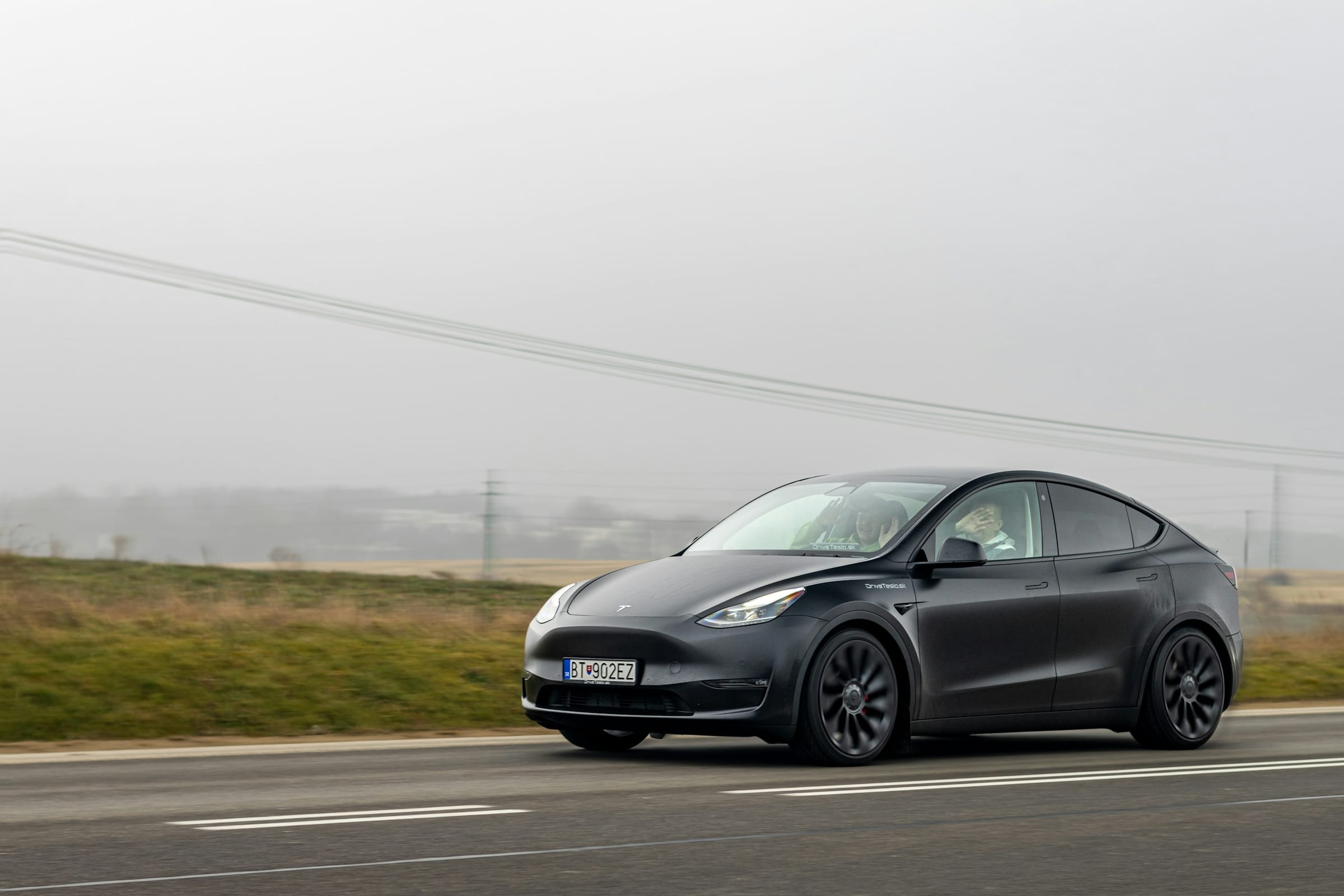 Black Tesla Model Y driving along a misty road